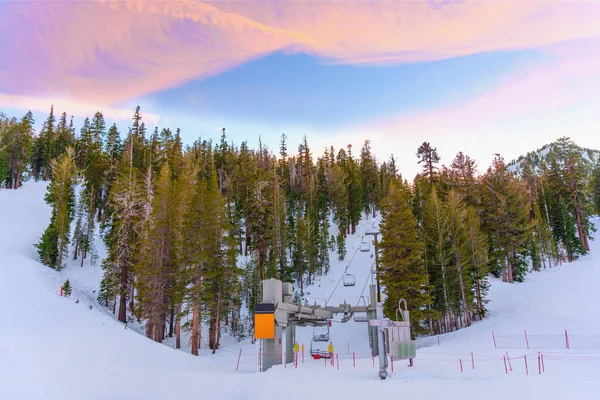 スキー場のリフトステーションでは 雪に覆われた斜面 雄大な夕日の空 背景に美しい松林が見えます — ストック写真