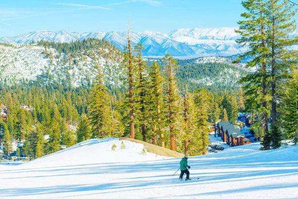 スキー場では 雪に覆われた山々 青空を背景に雪の斜面が降ります 遠くには木製のキャビンが見え 絵のように美しい冬の景色に加えています — ストック写真