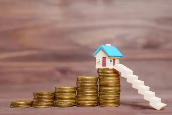 stock image Miniature staircase leading to a colorful toy house placed on top of a pile of coins, all set against a wooden background. Wise dream home investment and financial planning related concept.