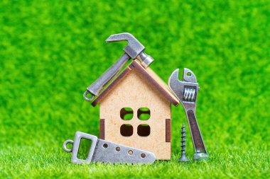 Minyatür ahşap ev modeli ve yeşil çimenlik arka planda izole edilmiş küçük ölçekli el aletleri. Küçük ev yenileme konsepti.