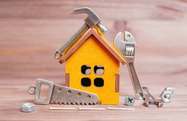 Minyatür ahşap bir ev modelinin etrafına yerleştirilmiş küçük, detaylı çelik el aletleri kopyaları ve bağlayıcılar. Küçük ev onarım konsepti.