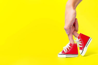 Parmakları yüksek kırmızı branda ayakkabılar giyen ve sarı arka planda yürüyen bacaklar gibi görünen eller. Yaratıcı ayakkabılar ve moda konsepti.