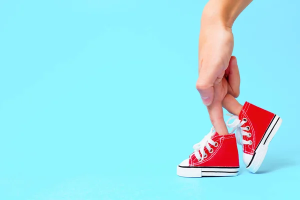 stock image Female hand with fingers dressed in red canvas trainers and arranged to look like legs against a light blue background with copy space. Creative advertising, design and fashion related concept.