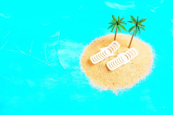 迷你版的构图让人想起热带岛屿的天堂 两张玩具棕榈树下的海滩日光浴床 放在一小堆沙子上 衬托着充满活力的蓝色背景 — 图库照片