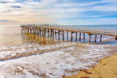 Malibu, California 'daki engin okyanusa uzanan ahşap iskele, dalgalar yavaşça kumlu sahili öpüyor..