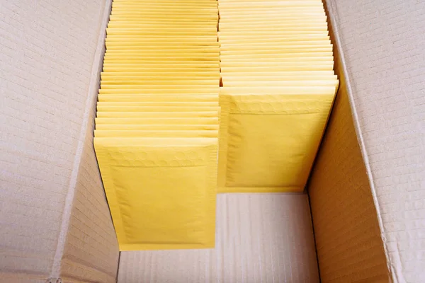 Cardboard box filled with yellow bubble mailers and some free space. Ordering e-commerce packaging supplies.