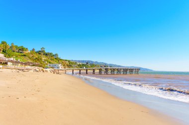 Malibu Sahili 'nin büyüleyici güzelliği kumlu kıyı şeridi manzarası sunuyor ve engin okyanusa uzanan ahşap iskele uzaktaki tepelerde yuva yapmış kıyı evleri..