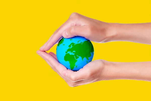 Cupped hands cradle a miniature green and blue globe isolated on yellow background. Environmental awareness and responsibility concept.