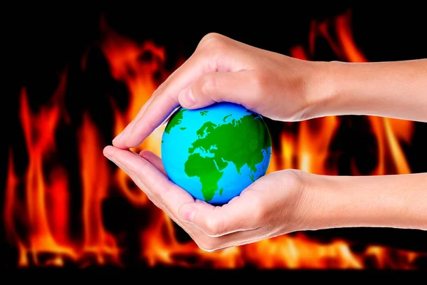 Cupped hands cradle a miniature green and blue globe against a backdrop of raging flames. Importance of global efforts towards sustainability, conservation and environmental consciousness.