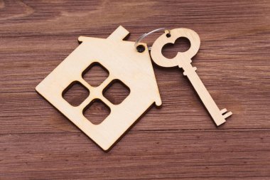 Düz ahşap anahtar, siyah ahşap arka planda ev şeklindeki anahtarlıkla eşleştirilmiş..