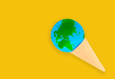Isınma ve iklim değişikliği kavramı: Minyatür küre, fotokopi alanı olan sarı arka planda izole edilmiş lezzetli bir dondurma külahının içine yerleştirilmiş..
