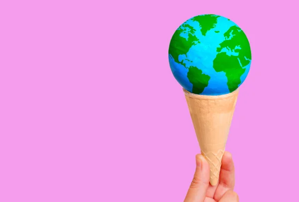 stock image Hand holding a miniature globe delicately placed inside a crispy waffle cone against a pink backdrop with copy space. Creative wanderlust and world exploration related concept.