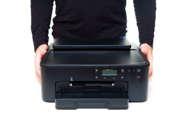 Siyah uzun kollu bir kişi, iki eli de temiz beyaz bir zemin üzerinde modern bir mürekkep püskürtme yazıcısı taşıyor. Kullanıcı dostu teknoloji ve taşınabilirlikle ilgili konsept.