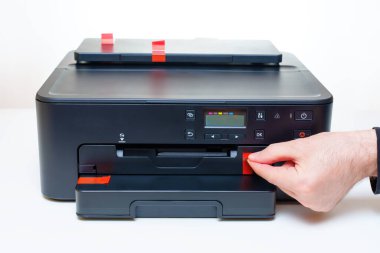 El, ofisteki beyaz bir masaya yerleştirilmiş yeni bir mürekkep püskürtme yazıcısının koruyucu taşıma etiketlerini dikkatlice soyar..