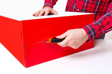 Kırmızı ve yeşil renkli kareli tişört giymiş birinin yan görüntüsü. Büyük kırmızı ve beyaz bir hediye kutusunu bıçak kullanarak dikkatlice açıyor. Noel hediyesi ve teknoloji.