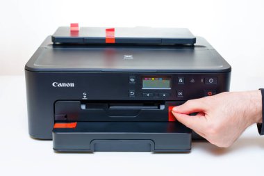 Kyiv, Ukrayna - 20 Temmuz 2023: Ofisteki beyaz bir masadaki yeni Canon mürekkep jeti yazıcısının koruyucu taşıma etiketlerini dikkatlice elden çıkarıyor.