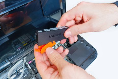 Kyiv, Ukrayna - 20 Temmuz 2023: Eller, kurulumdan önce Canon mürekkep jeti yazıcı kartuşundan turuncu koruyucu kapsülü yavaşça çıkarın.