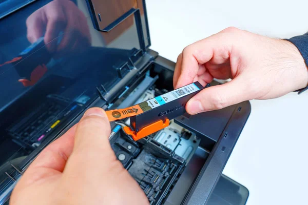 Kyiv, Ukrayna - 20 Temmuz 2023: Kurulumdan önce erkek ellerinin yeni bir Canon mürekkep jeti yazıcı kartuşundan koruyucu etiketi çıkarmasının ayrıntılı görünümü.
