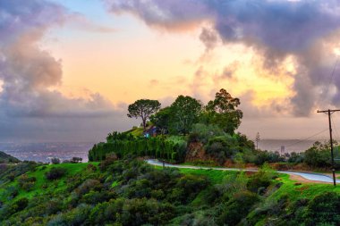 Runyon Kanyonu 'nun yeşil tepeleri Los Angeles' ın şehir manzarasına ve günbatımının yakıcı gökyüzüne karşı kurulmuştur..