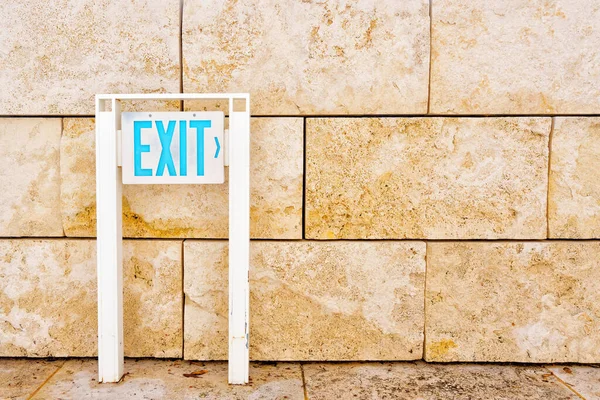 EXIT sign placed next to a wall constructed from sturdy stone slabs.