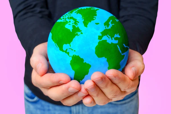 Close-up view of person\'s hands extending to present a verdant globe isolated on pink background. Shared responsibility and unity for the Earth protection.