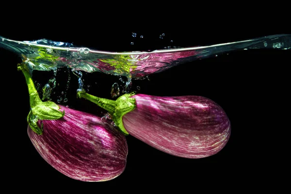 Close-up of a pair of graffiti eggplants dropped in Water with splashes against black background.