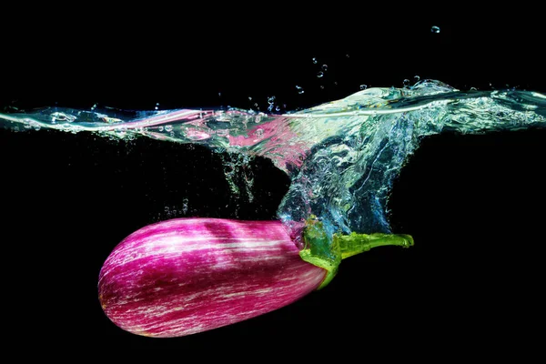 Close-up of a Sicilian eggplant dropped underwater with splashes on black.