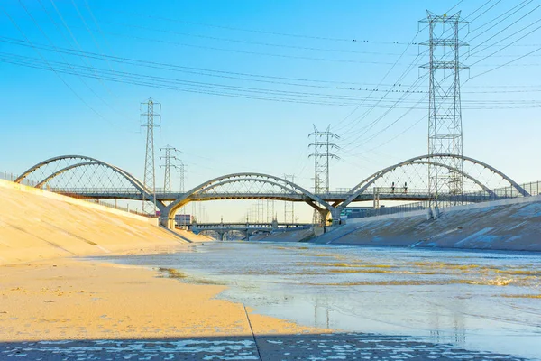 Los Angeles Nehri 'nin resimli görüntüsü ikonik 6. Cadde Köprüsü ve elektrik hatlarından oluşan bir ağ tarafından çerçevelenmiş..