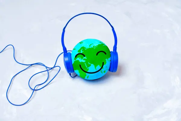 Smiling globe character immersed in listening with blue headphones isolated on a concrete background. International music discovery concept.