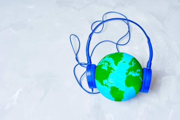 Globe model wearing blue headphones isolated on concrete background. Global music streaming services related concept.
