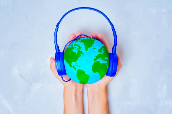 Top view of cupped hands holding a green and blue globe model with headphones on top. Foreign language learning related concept.