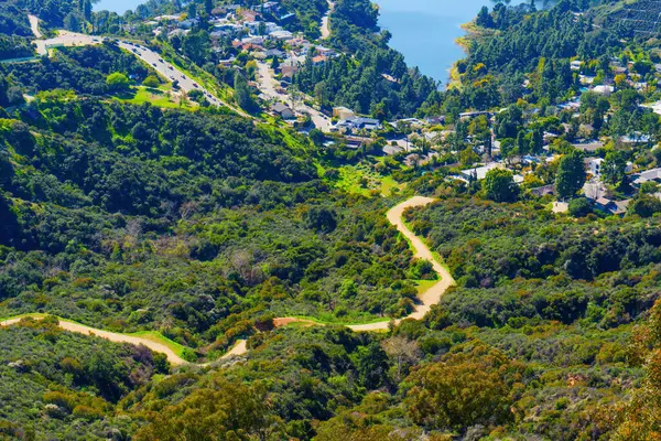 Inviting path winds through a verdant hillside, guiding the way to the serene Hollywood Reservoir in Los Angeles, a peaceful retreat for nature lovers and hikers.