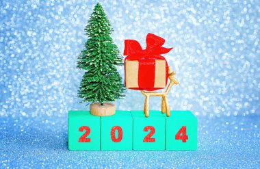 Minyatür pırıl pırıl yeni yıl 2024 arkaplanı yeşil ahşap harf bloklarından, oyuncak noel ağacından, küçük geyik heykelciğinden ve süslü bir hediye kutusundan düzenlenmiş..