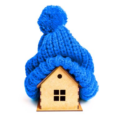 Beyaz üzerine izole edilmiş zarif mavi örgü bir şapkayla süslenmiş küçük tahta bir ev. Yaratıcı ev yalıtımı ve mevsimsel hazırlık konsepti.