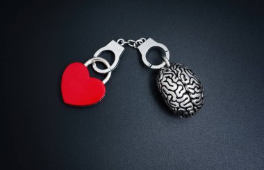 İnsan beyni modeli ve kırmızı kalp şeklinde bir kilit siyah kelepçelerle birbirine bağlanır. Düşünce ve duygunun sembolik sinerjisi.
