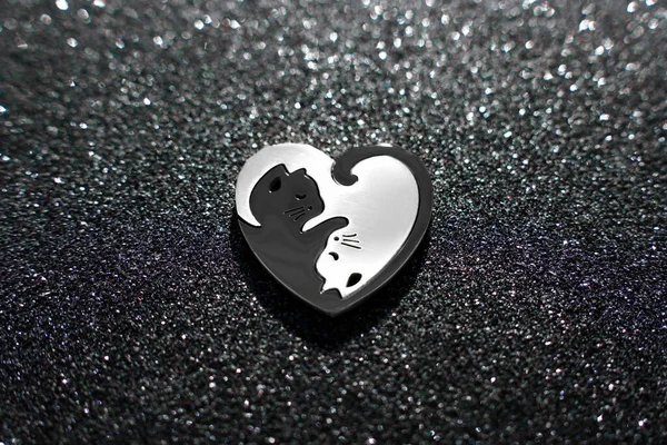 Close-up view of a heart-shaped puzzle made of two matching silver and black cats, placed on a sparkling background.