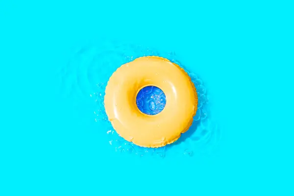 Top-view of a yellow swim ring drifting on the water surface, set against a cheerful blue backdrop. Summer related background.