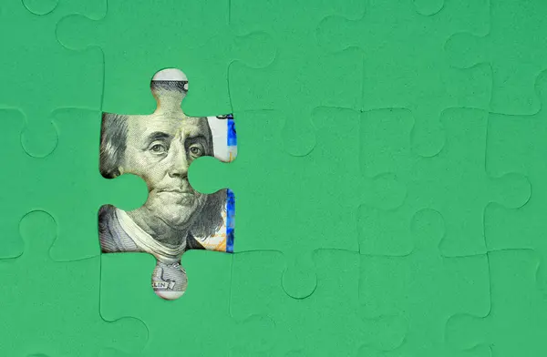 Green jigsaw puzzle background revealing some parts of a hundred dollar bill. Building wealth through hard work and financial planning.