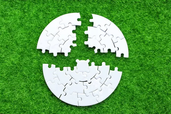 Close-up of a circular white puzzle split into three parts, resting on vibrant green grass. Unity, harmony and nature related concept.