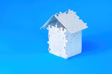 Beyaz yapboz kağıtları mavi arka planda izole edilmiş kalça çatılı küçük bir ev modeline yerleştirilmiş..