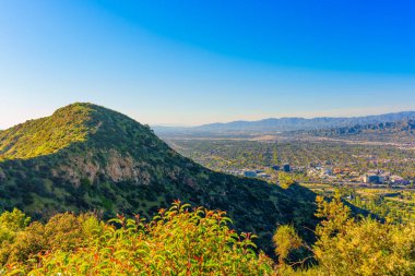 Los Angeles manzarası uçsuz bucaksız yeşil tepeler, dağlar ve mavi gökyüzü ile çevrili..