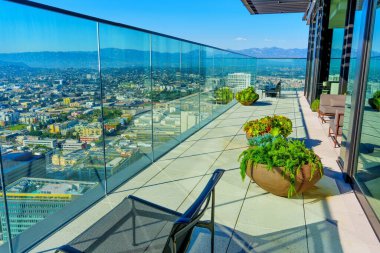 Geniş balkon, saksıları, modern mobilyaları ve cam cepheleriyle sakin bir vahaya dönüşerek Los Angeles manzarası sunuyor..