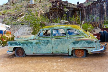 Nelson, Nevada - 15 Nisan 2024: Paslı klasik Chrysler arabası terk edilmiş altın madeninin yıpranmış binalarının önüne park edilmiş.