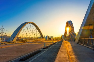 Günbatımında çekilen modern kemer köprüsünde, sıcak güneş ışığı kemerlerin arasından süzülerek, yapının üzerinde ışık ve gölge etkileşimi oluşturur..