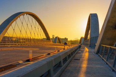 Şehir siluetine giden modern bir köprünün üzerinde çarpıcı bir günbatımıyla çekilen sakin bir şehir akşamı..