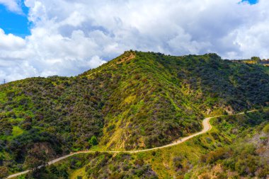 Runyon Kanyon Parkı 'nın dolambaçlı yolunda yürüyen insanlar, mavi gökyüzünün altında, beyaz bulutlu resimli tepelerin yanında..