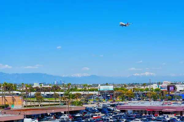 Los Angeles, Kaliforniya - 9 Nisan 2024: Los Angeles Havaalanı ekonomi parkına parketmiş dağlar, mavi gökyüzü ve arka planda inmek üzere olan bir uçak.