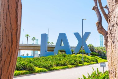 Los Angeles, Kaliforniya - 8 Nisan 2024: Ağaç gövdeleri tarafından çerçevelenmiş yemyeşil bir çimenlikte LAX işareti.