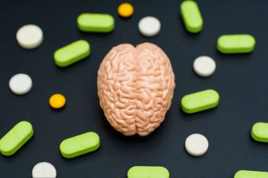 Çamur beyin modeli, siyah bir yüzeyde çeşitli renklerde haplarla çevrili. Ruh sağlığı, tıbbi tedavi, nörobilim ve farmakoloji kavramı.