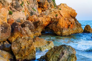 Playa de la Mora 'da yumuşak ışık altında kıyı şeridi yakınlarında canlı turuncu kayalar..